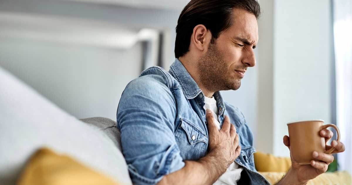 Man holding his chest, appearing to experience discomfort while holding a cup