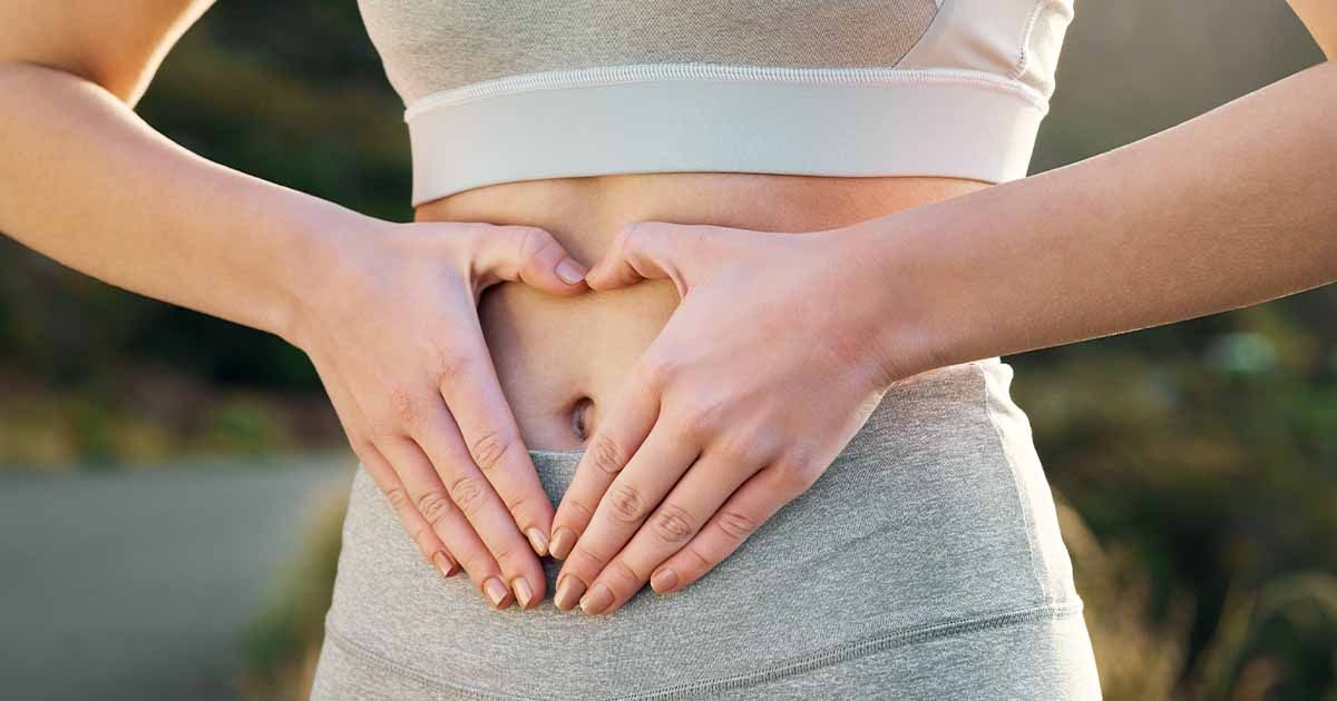 Woman in workout clothing with hands in shape of heart on stomach.