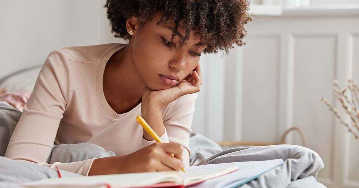 Woman laying on bed, writing in a journal.