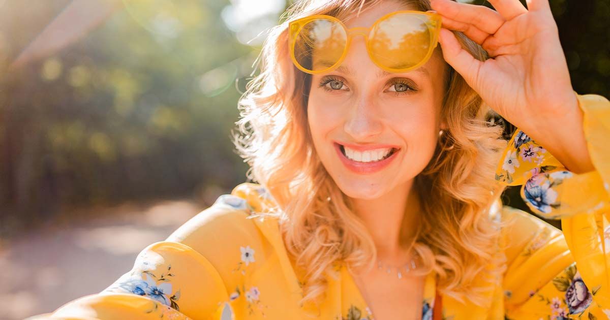 Woman smiling in the sun with yellow shirt and sunglasses.